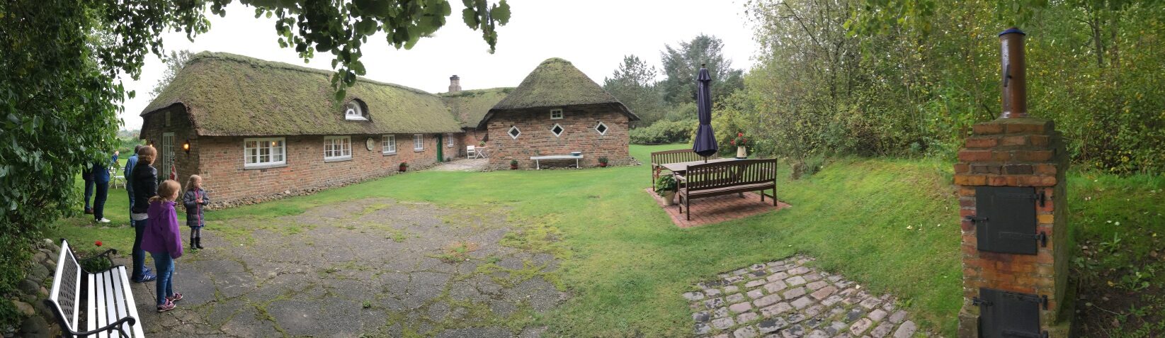 Panoramafoto af gårdspladsen på Silkjær med den lange stråtækte længe og det runde udhus