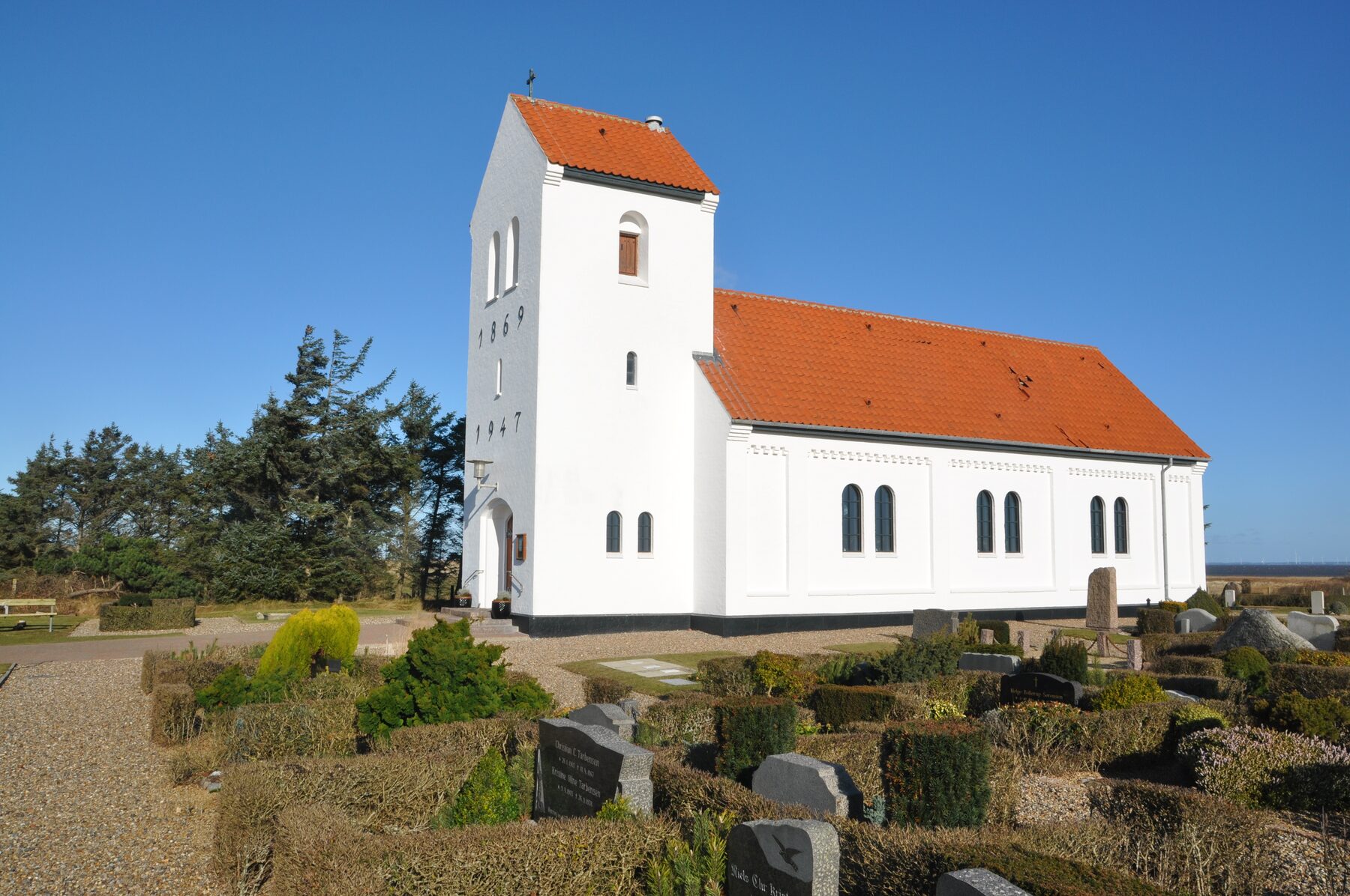 Haurvig Kirke: hvidkalket kirke med rødt tegltag og tårn med årstallene 1869 og 1947, omgivet af kirkegård i klitlandskab