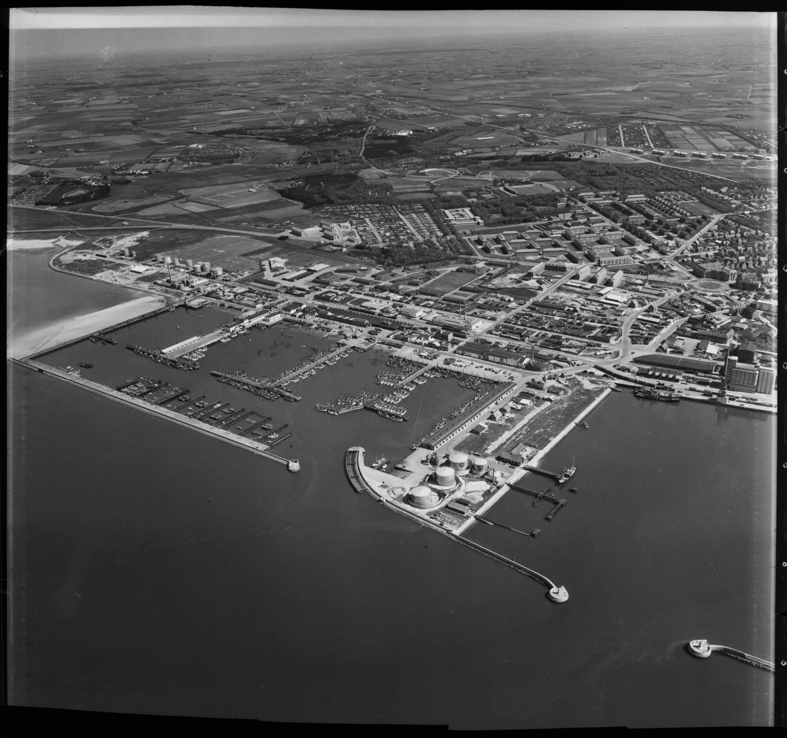 Luftfoto af Esbjerg fiskerihavn 1956: kuttere i tætte rækker langs broerne, moler, olietanke og byen bagved