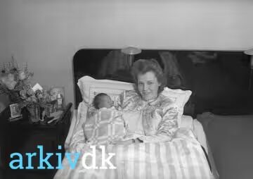 Kvinde i barselsseng med et nyfødt barn ved siden af sig, natbord med blomster og fotografier, 1944