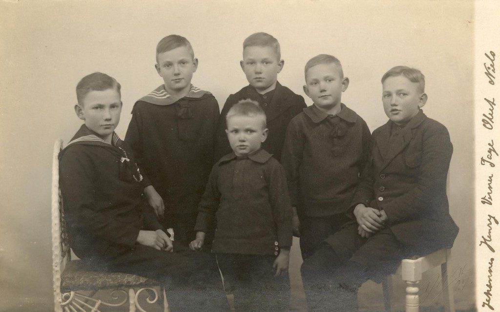 Atelierfotografi af seks drenge i mørkt tøj, to i matrostrøjer, den mindste stående forrest i midten; langs højre kant er navnene Johannes, Henry, Verner, Tage, Oluf og Niels skrevet med blæk